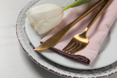 Stylish table setting with cutlery and tulip on white marble background, closeup