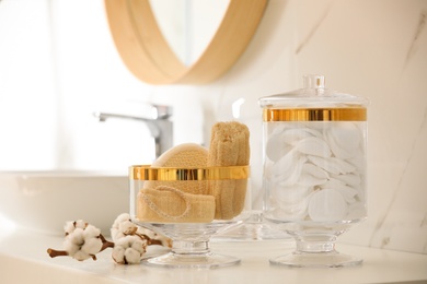 Photo of Jars with cotton pads and loofah sponges on countertop in bathroom