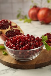 Photo of Ripe juicy pomegranate grains in bowl and green leaves on white marble table