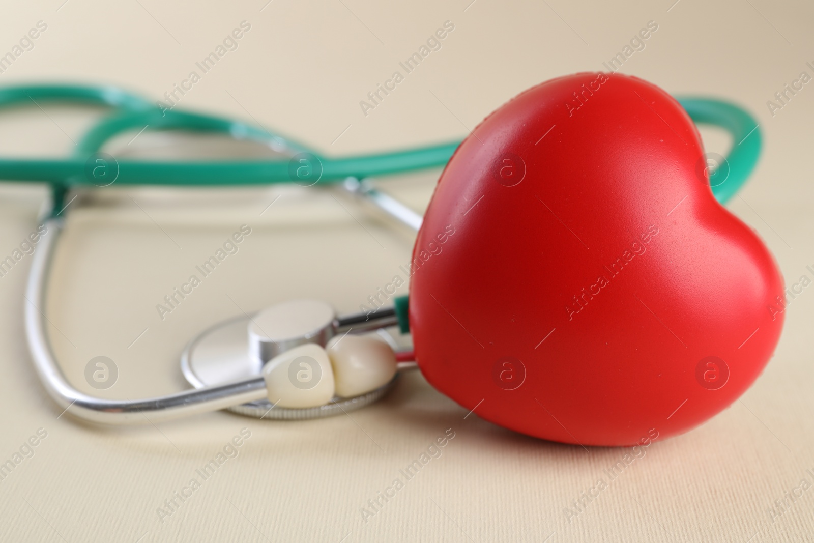Photo of Stethoscope and red heart on beige background, closeup