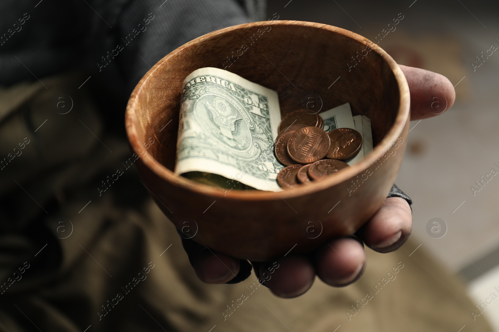 Photo of Poor homeless man holding bowl with donations on blurred background, closeup