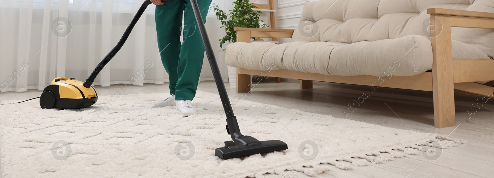 Image of Dry cleaner's employee hoovering carpet with vacuum cleaner in room, closeup. Banner design