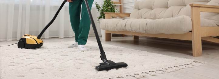 Dry cleaner's employee hoovering carpet with vacuum cleaner in room, closeup. Banner design