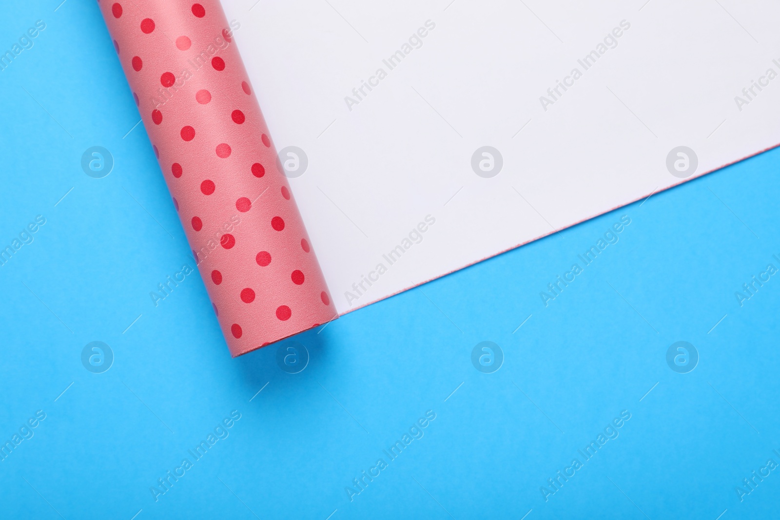Photo of Roll of polka dot wrapping paper on light blue background, top view. Space for text