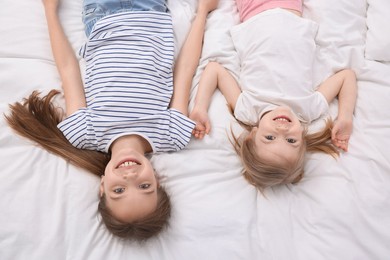 Photo of Cute little sisters on bed, top view