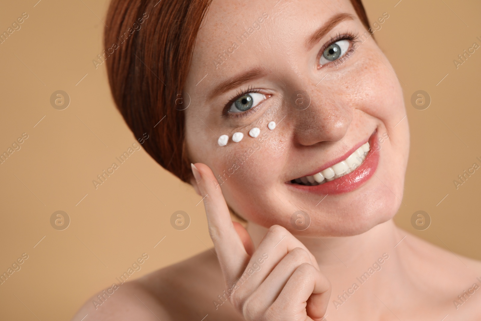 Photo of Smiling woman with freckles and cream on her face against beige background, closeup