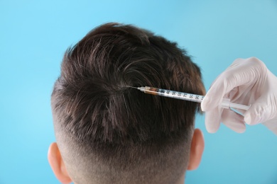 Young man with hair loss problem receiving injection on color background