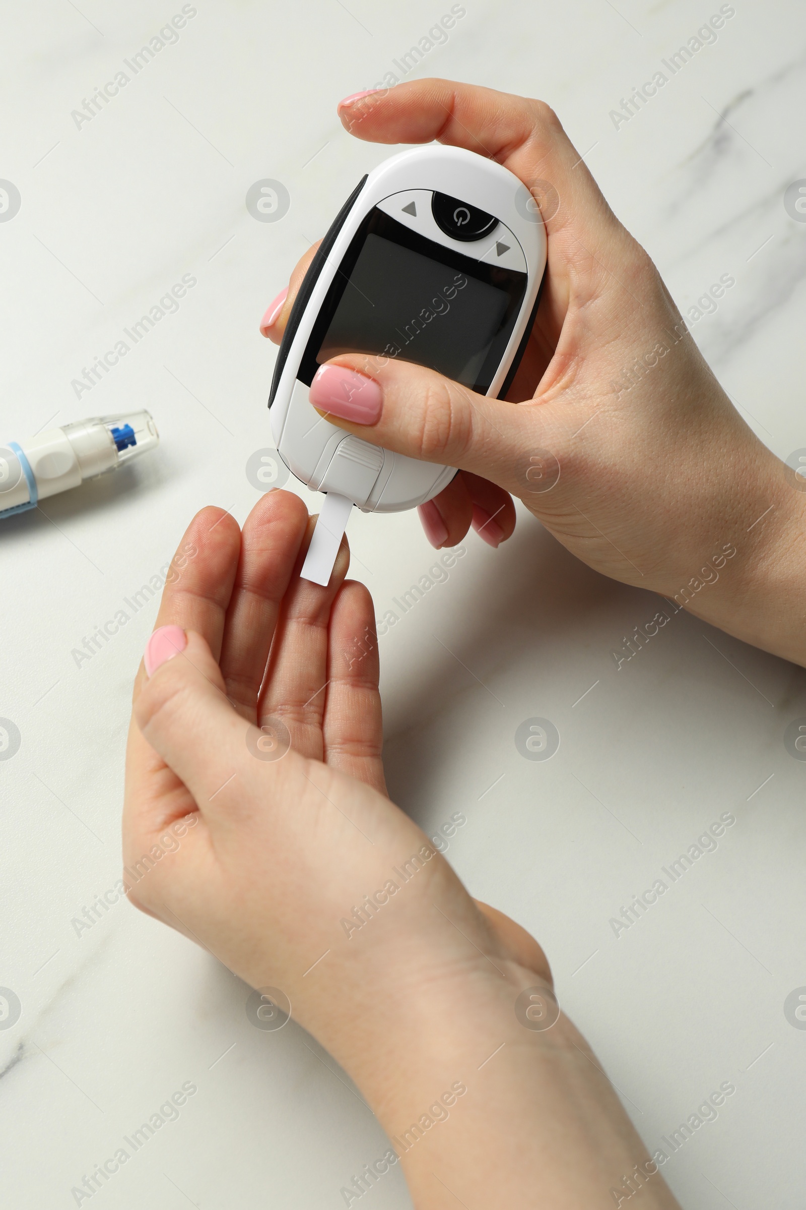 Photo of Diabetes. Woman checking blood sugar level with glucometer at white marble table, top view