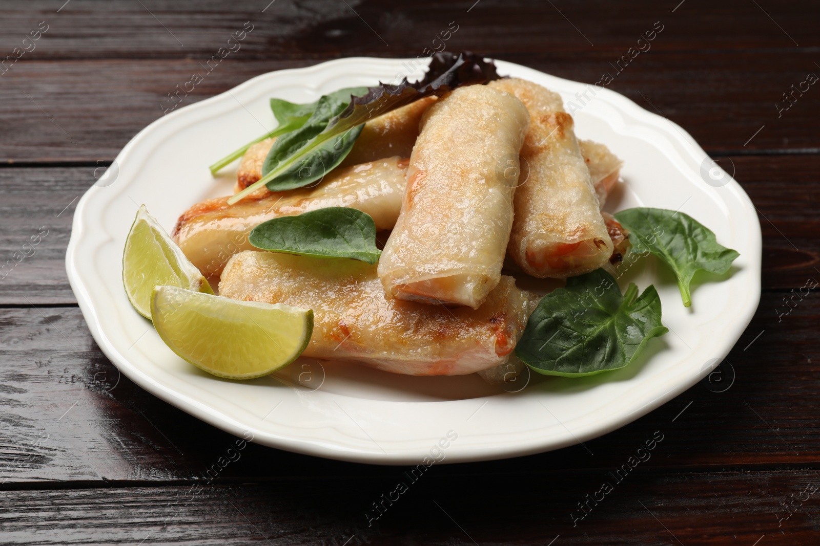 Photo of Plate with tasty fried spring rolls, spinach and lime on wooden table, closeup
