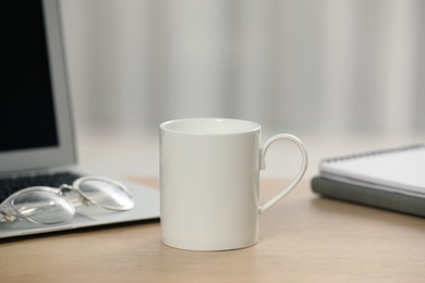 Photo of White ceramic mug, glasses and laptop on wooden table at workplace