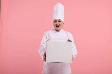 Photo of Happy professional confectioner in uniform holding cake box on pink background