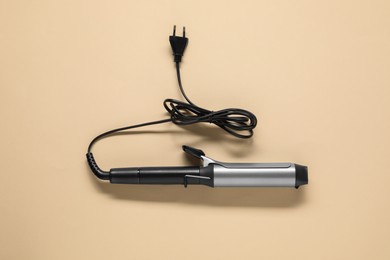 Photo of Curling iron on beige background, top view