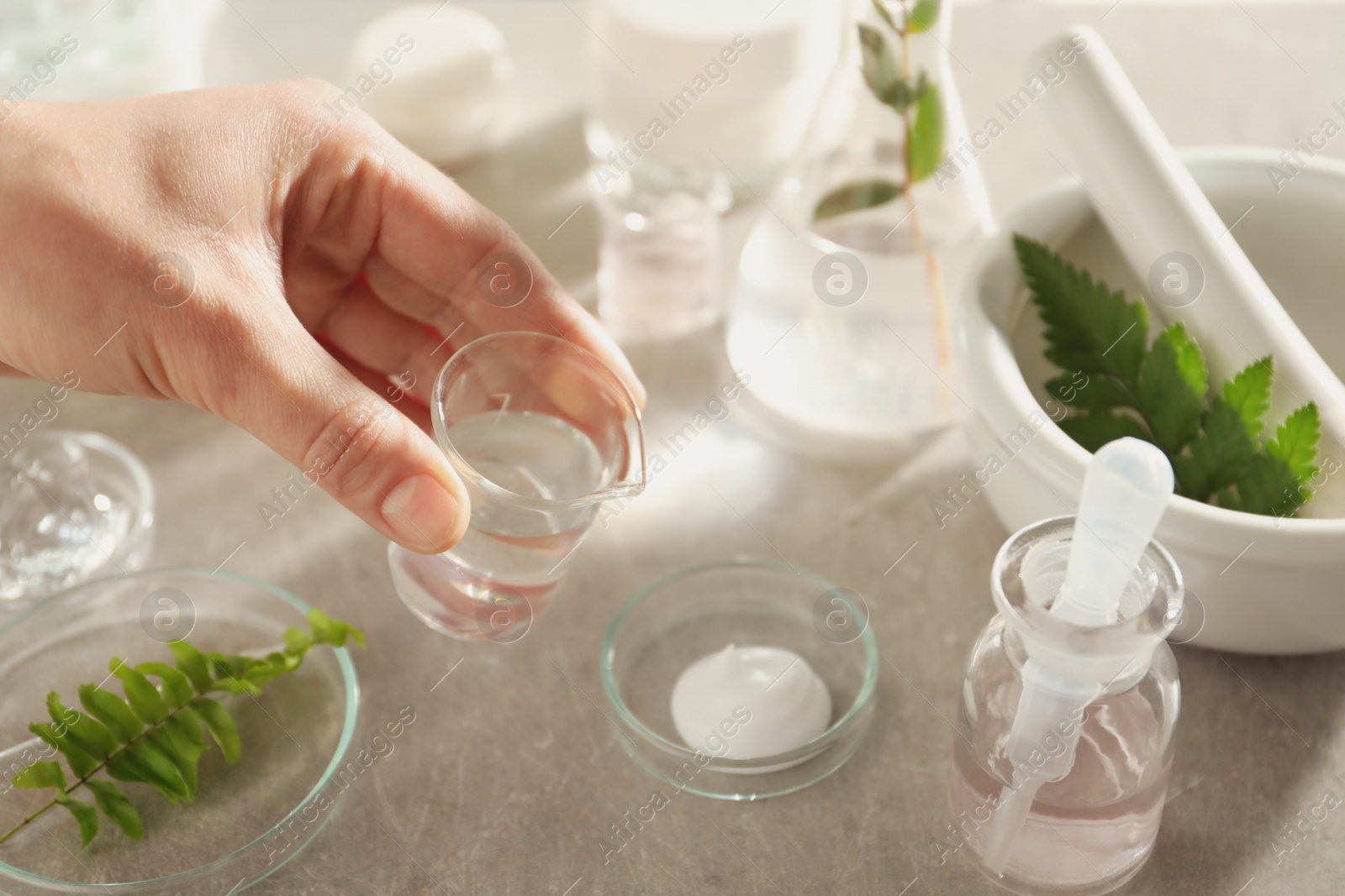 Photo of Scientist making cosmetic product at grey table, closeup