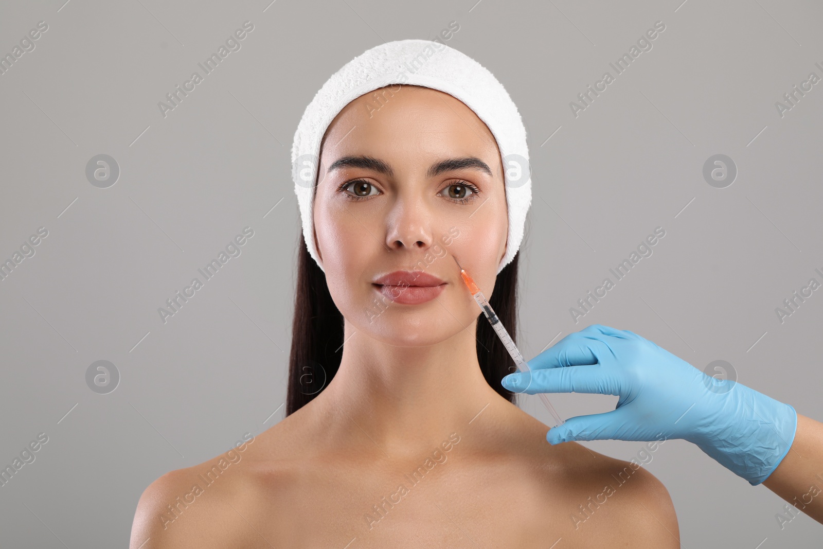 Photo of Doctor giving facial injection to young woman on light grey background. Cosmetic surgery