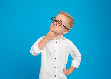 Portrait of cute little boy in glasses on light blue background