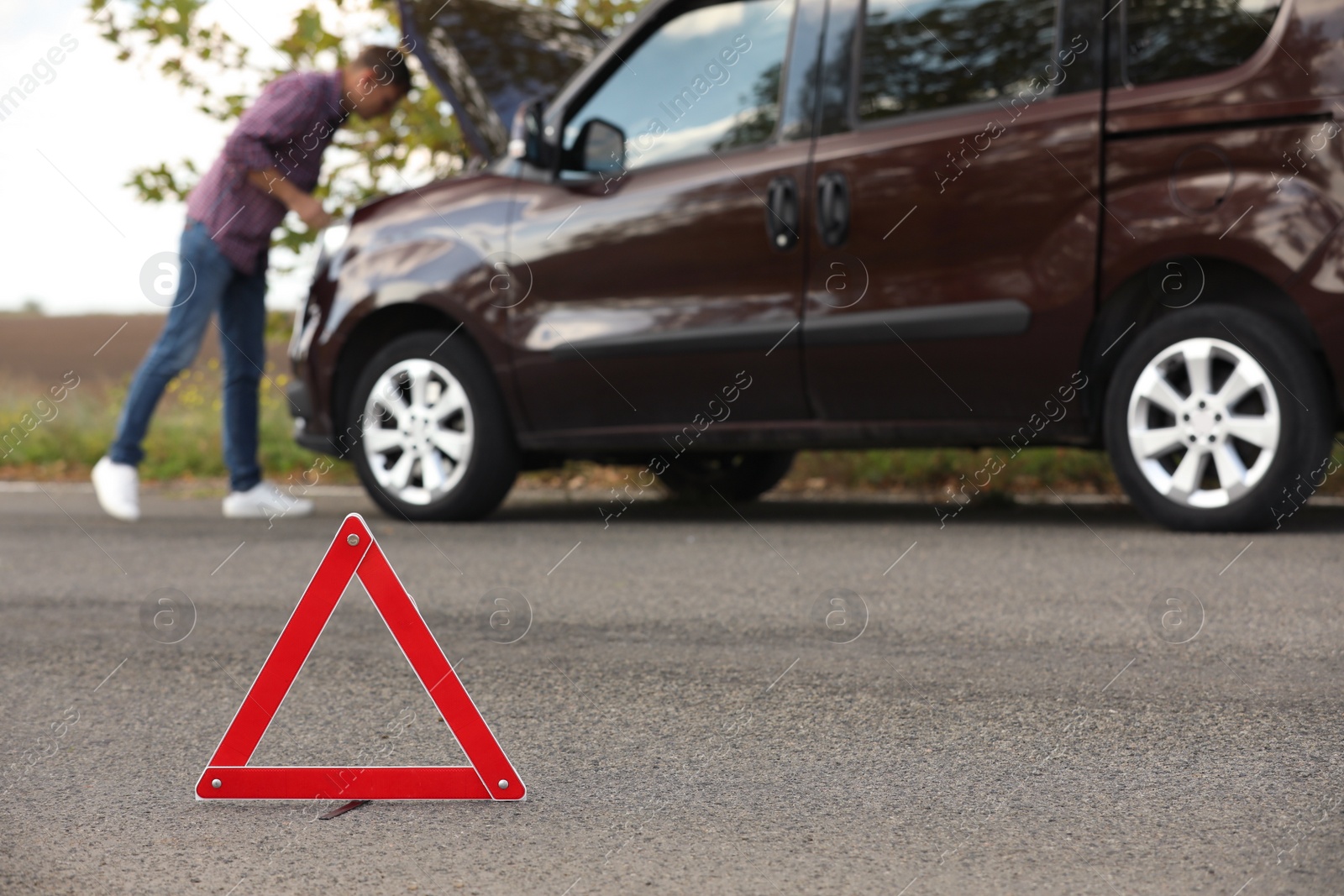 Photo of Emergency stop sign and driver near broken car on road. Auto insurance