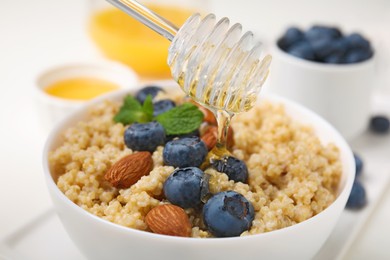 Photo of Pouring honey onto delicious cooked quinoa with almonds and blueberries in bowl, closeup