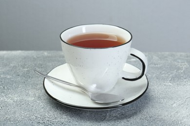 Photo of Aromatic tea in cup and spoon on grey table