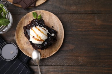 Photo of Tasty brownies served with ice cream and caramel sauce on wooden table, flat lay. Space for text
