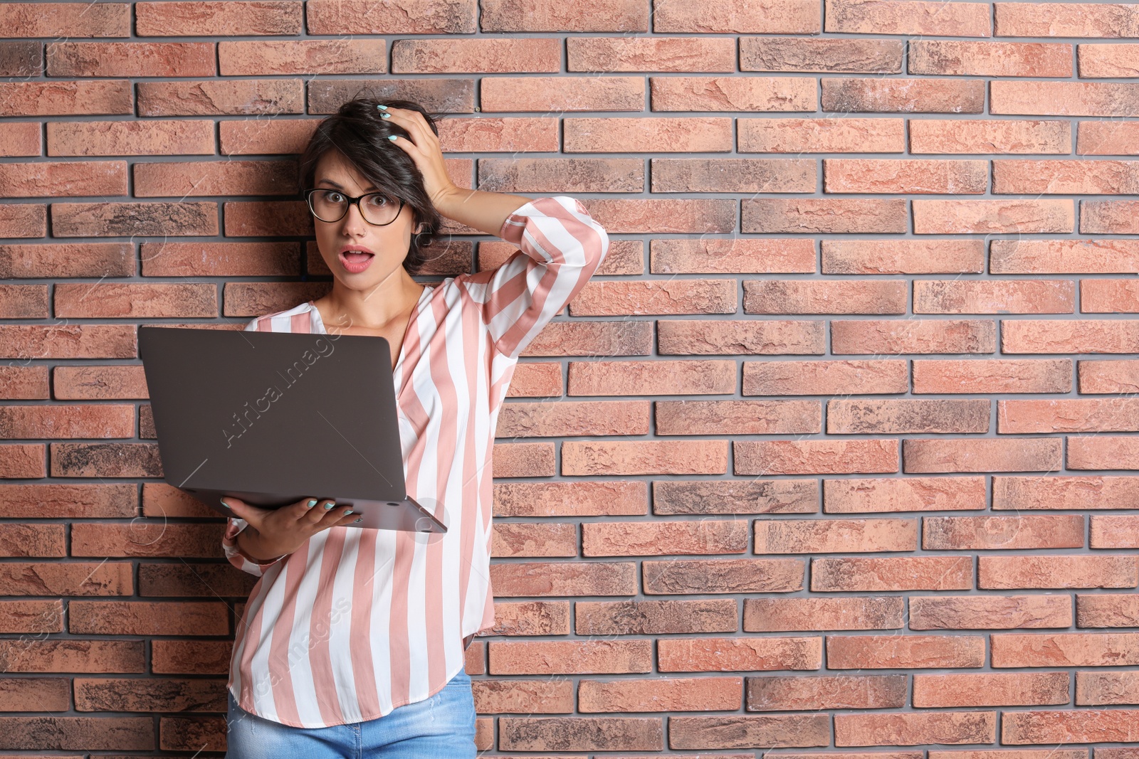 Photo of Young woman with modern laptop on brick wall background