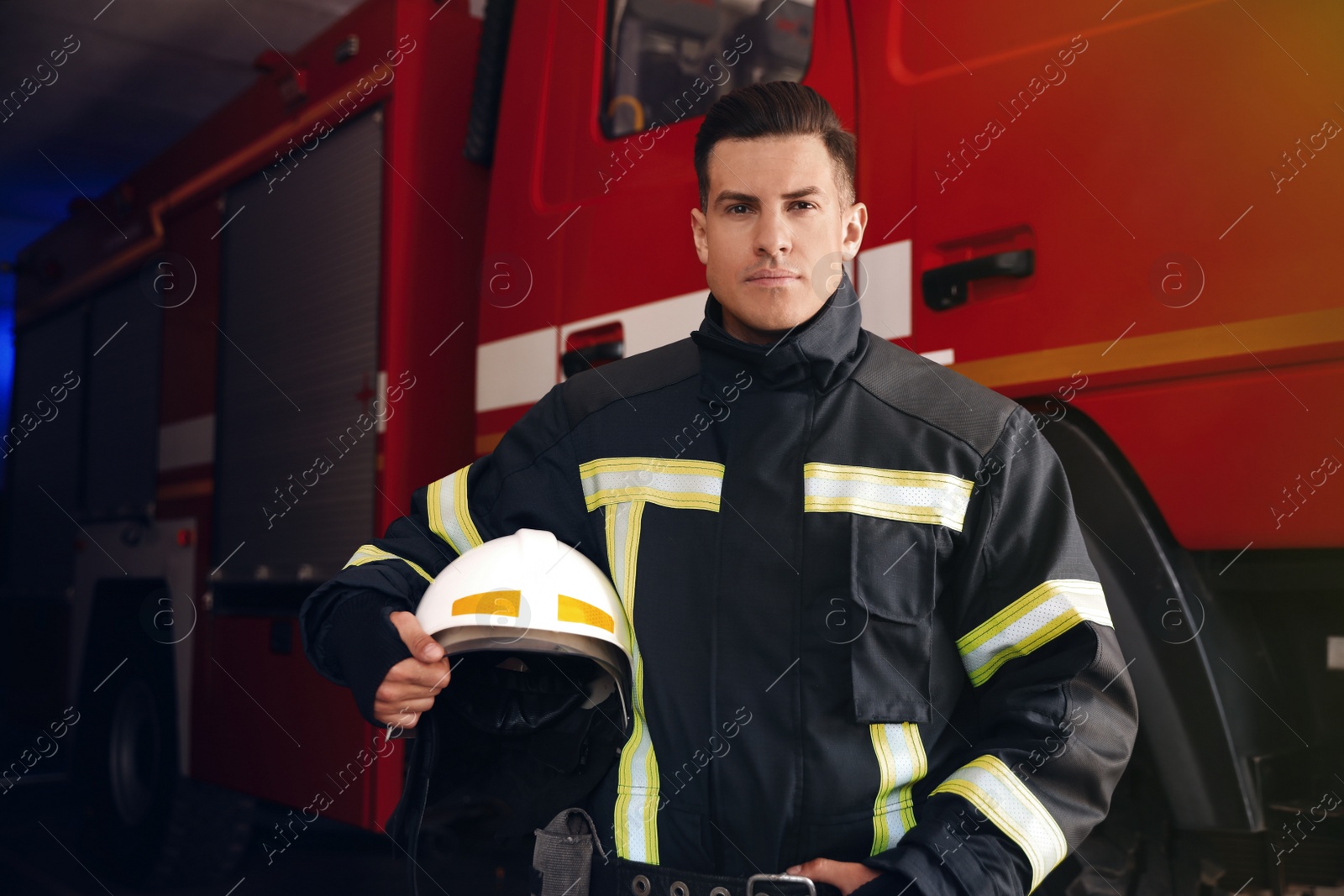 Photo of Portrait of firefighter in uniform with helmet near fire truck at station