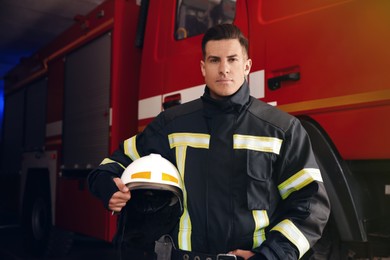 Photo of Portrait of firefighter in uniform with helmet near fire truck at station