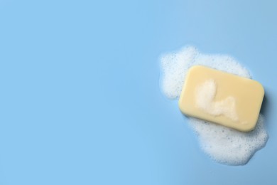 Photo of Soap and fluffy foam on light blue background, top view. Space for text