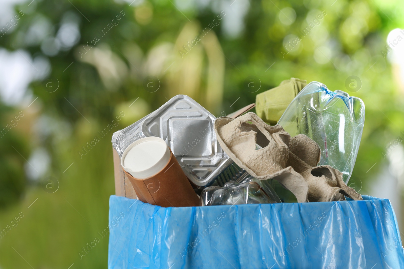 Photo of Trash bin with garbage on blurred background, space for text. Recycling problem