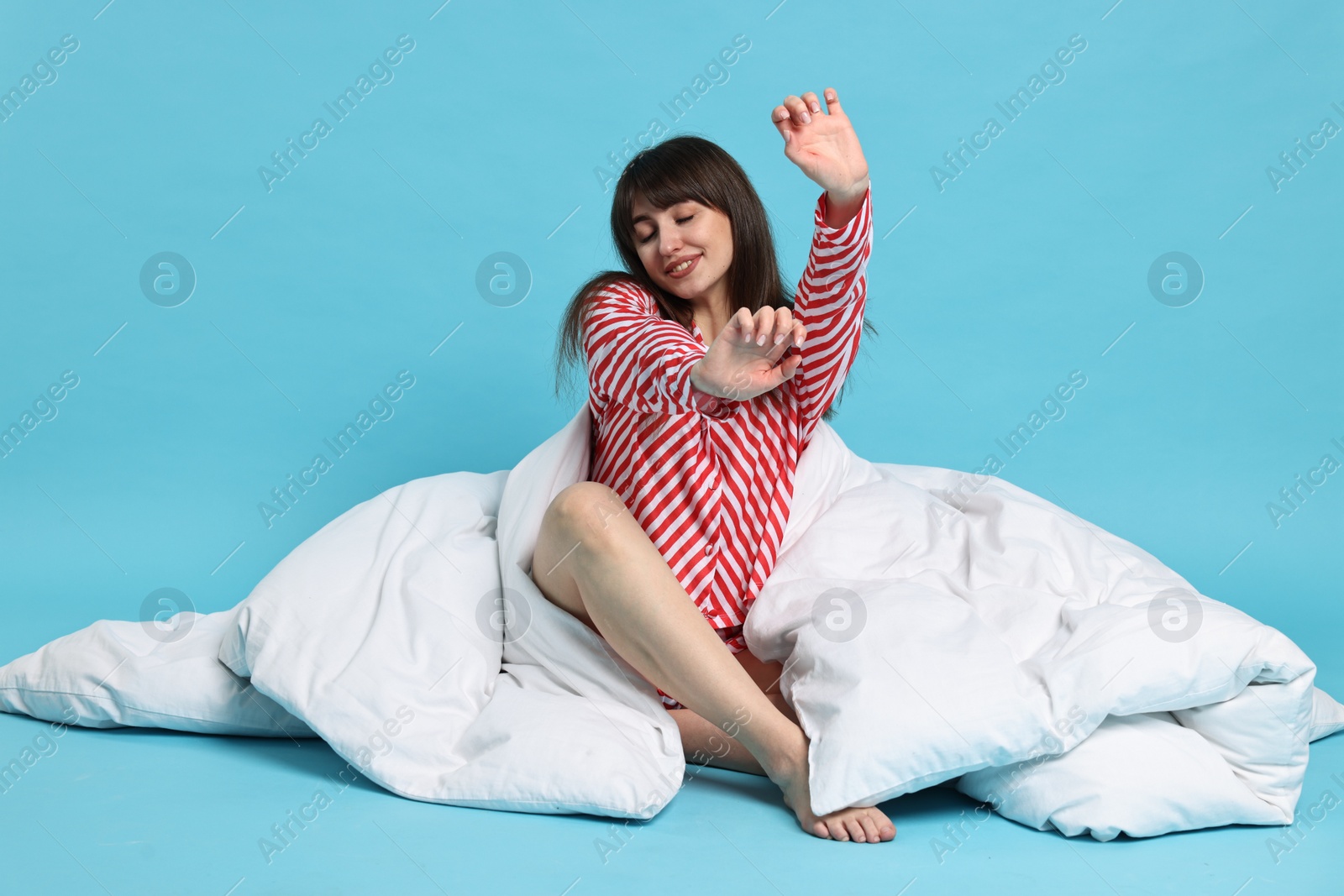 Photo of Happy woman with pyjama and blanket stretching on light blue background