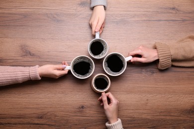 Photo of Women with cups of coffee at wooden table, top view