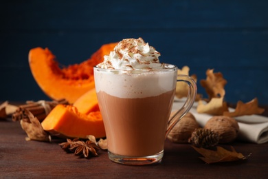 Photo of Delicious pumpkin latte and ingredients on brown wooden table, closeup