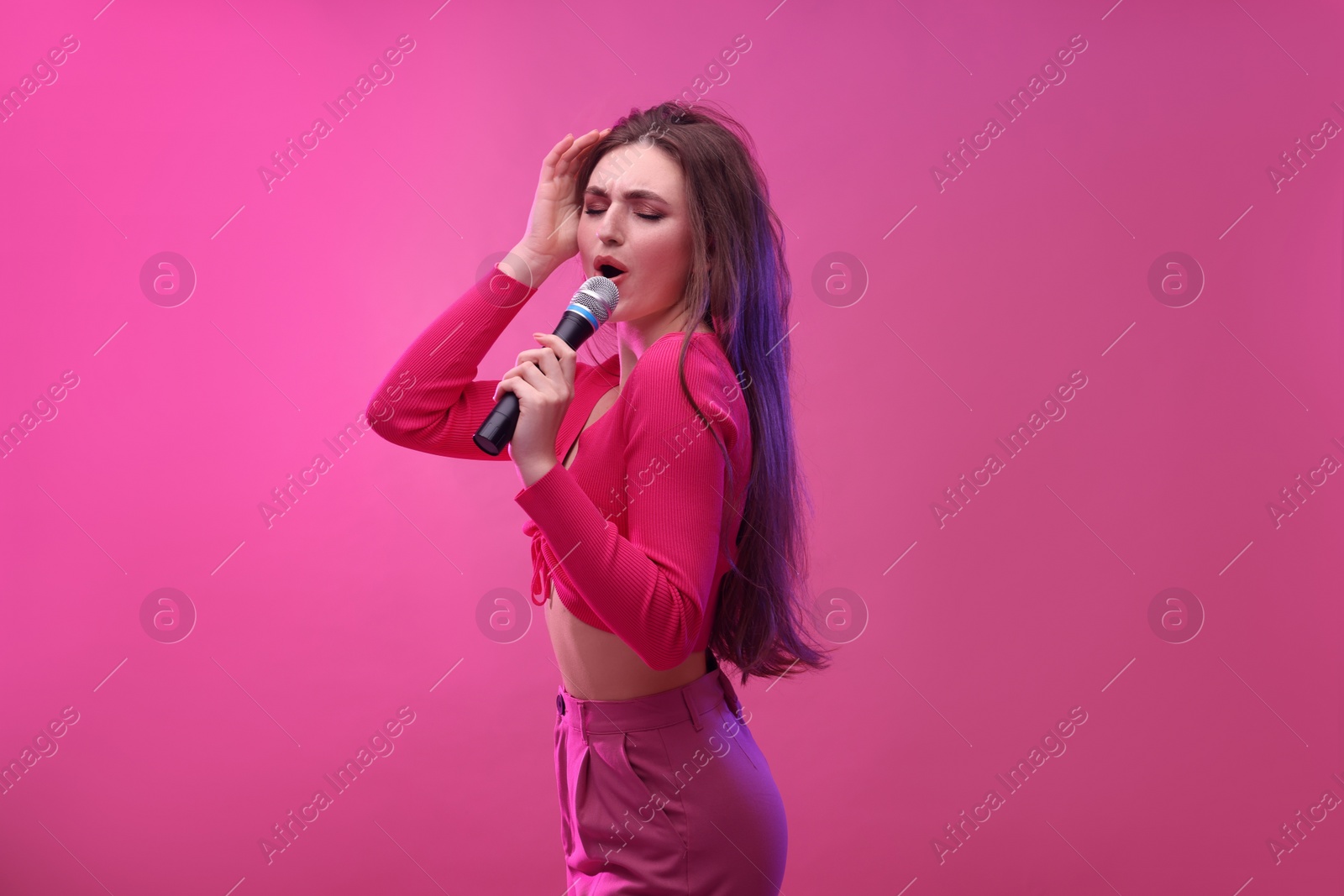 Photo of Emotional woman with microphone singing on pink background