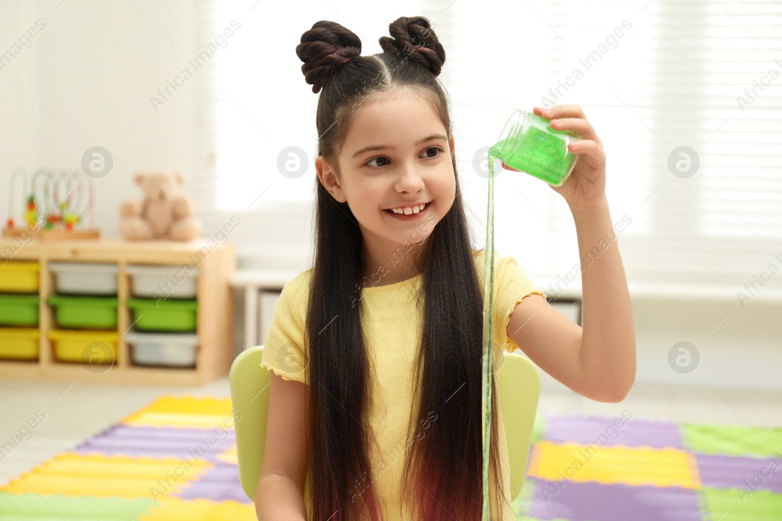 Photo of Little girl pouring slime from jar in room