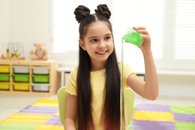 Little girl pouring slime from jar in room