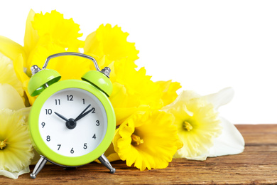 Green alarm clock and spring flowers on wooden table against white background. Time change