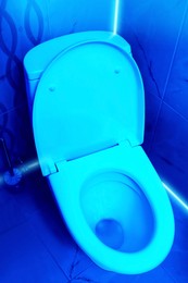 Image of Toilet bowl in public restroom lit with UV blue light