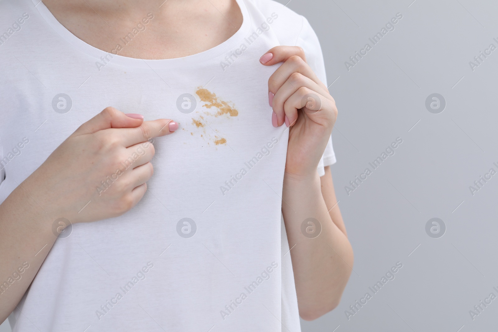 Photo of Woman showing stain on her t-shirt against light grey background, closeup. Space for text