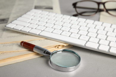 Photo of Magnifying glass, keyboard and stack of newspapers on grey table. Job search concept