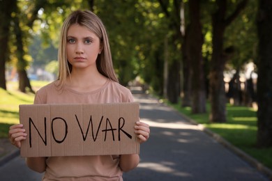 Photo of Sad woman holding poster with words No War in park. Space for text