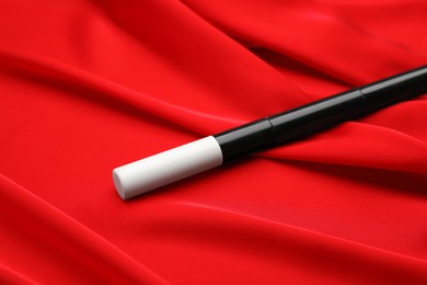 Photo of Beautiful black magic wand on red fabric, closeup