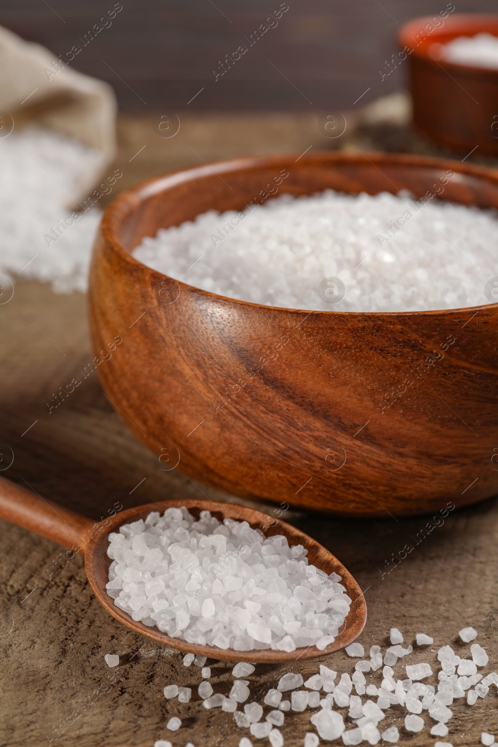 Photo of Bowl and spoon with natural sea salt on wooden table, closeup