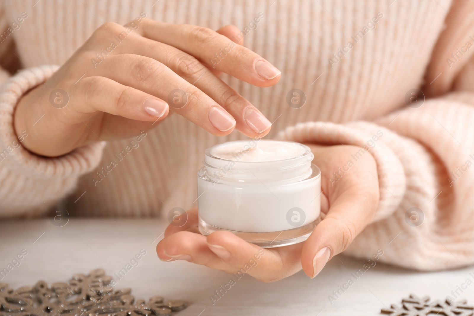 Photo of Woman holding jar of cream at light table, closeup. Cosmetic product for winter