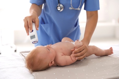 Photo of Doctor measuring temperature of little baby with non-contact thermometer in clinic, closeup. Health care