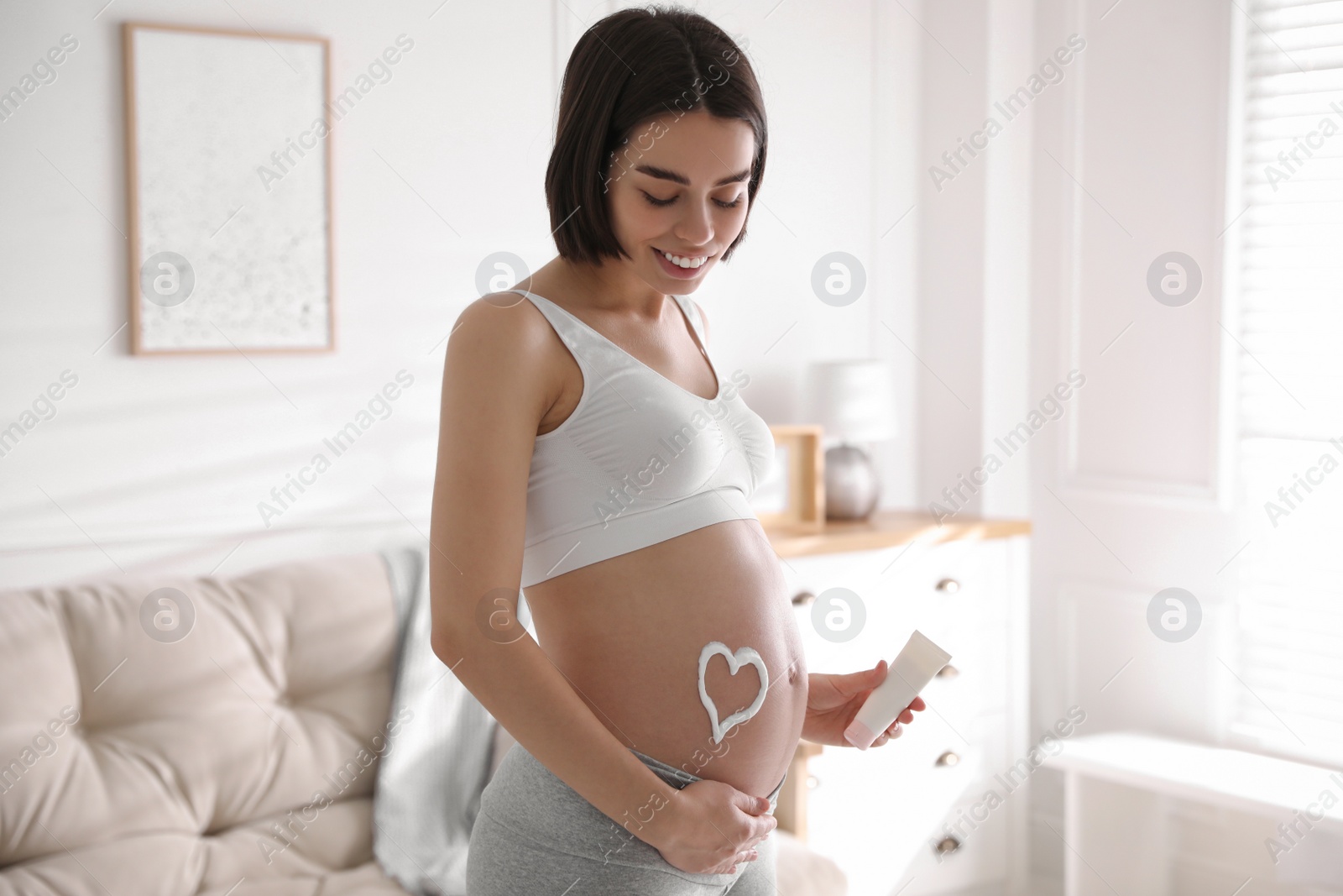 Photo of Young pregnant woman with cosmetic product at home