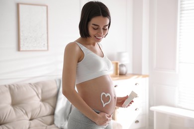 Photo of Young pregnant woman with cosmetic product at home