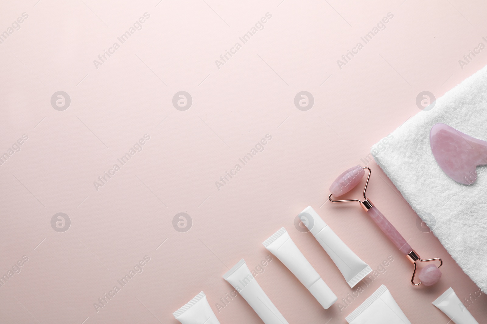 Photo of Natural face roller, gua sha tool, cosmetic products and towel on pink background, flat lay. Space for text