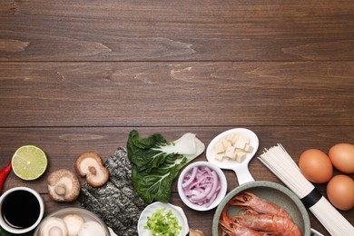 Photo of Cooking delicious ramen soup. Different ingredients on wooden table, flat lay. Space for text