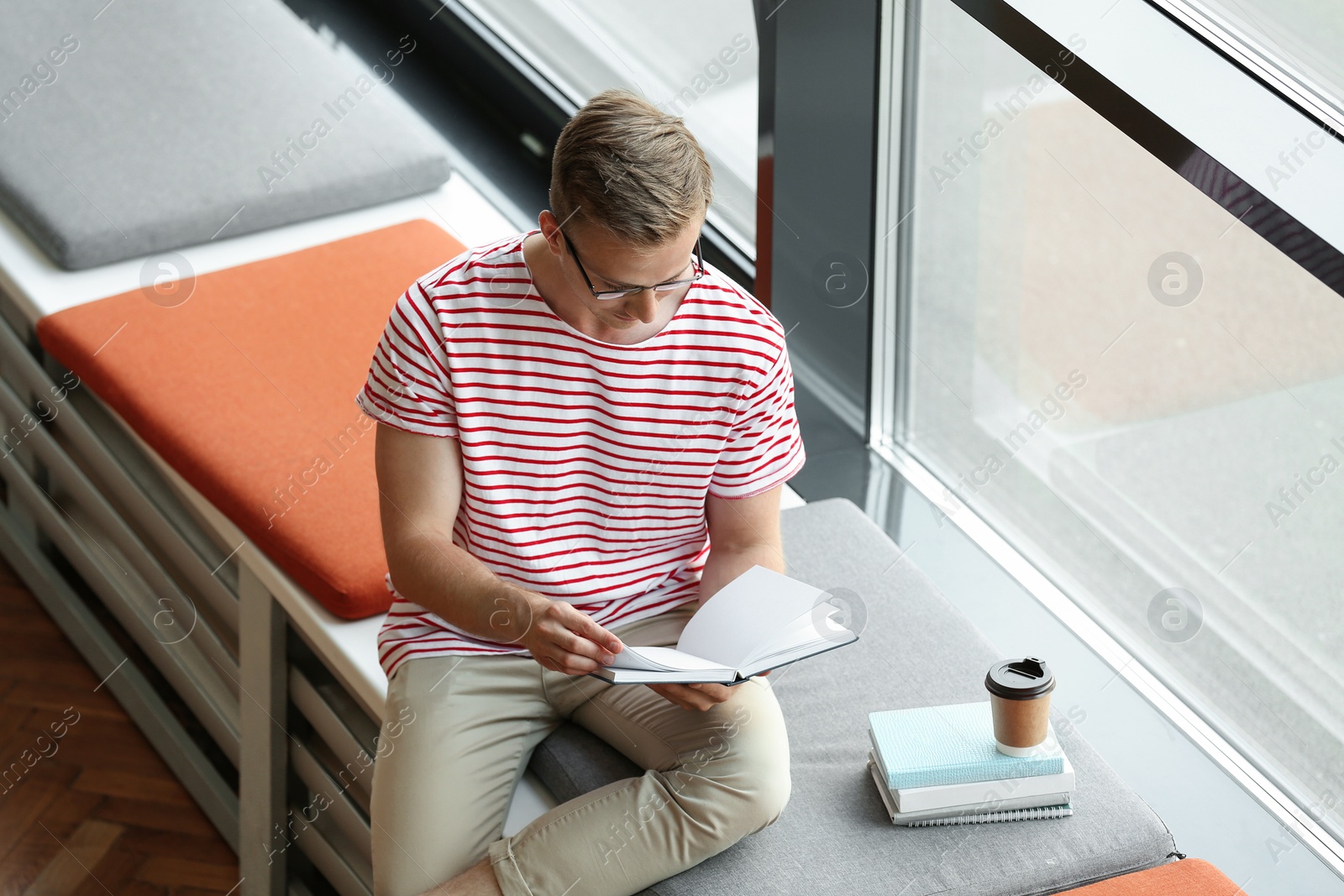 Photo of Young man reading book near window in library