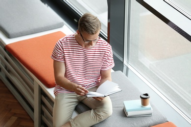 Young man reading book near window in library