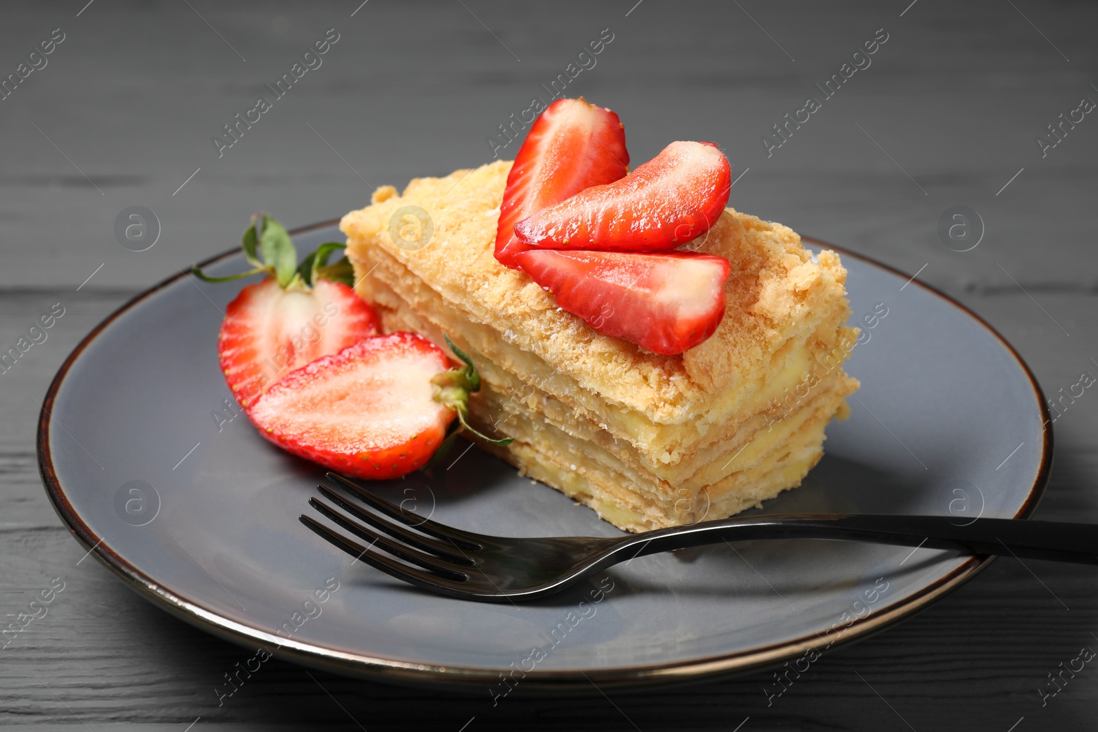 Photo of Piece of delicious Napoleon cake with strawberries on grey wooden table, closeup